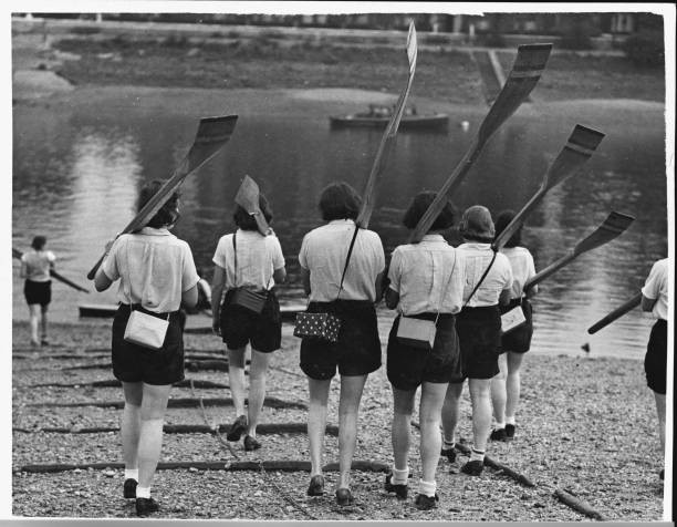Women's rowing crew carry their oars down to the river with gas ma- Old Photo